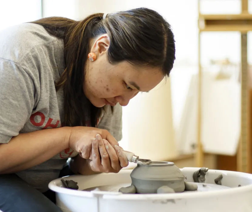 "An artist focusing intently while shaping a clay pot on a pottery wheel, working with great precision in an art studio.