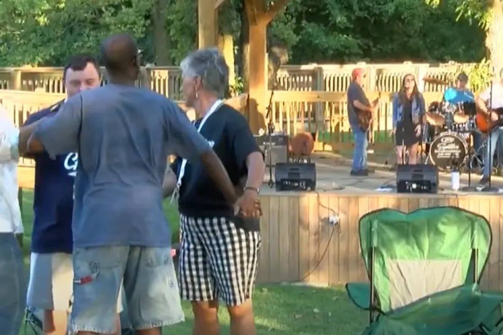 A diverse group of individuals gathered around a stage in a park, engaged in conversation and enjoying the outdoor event.