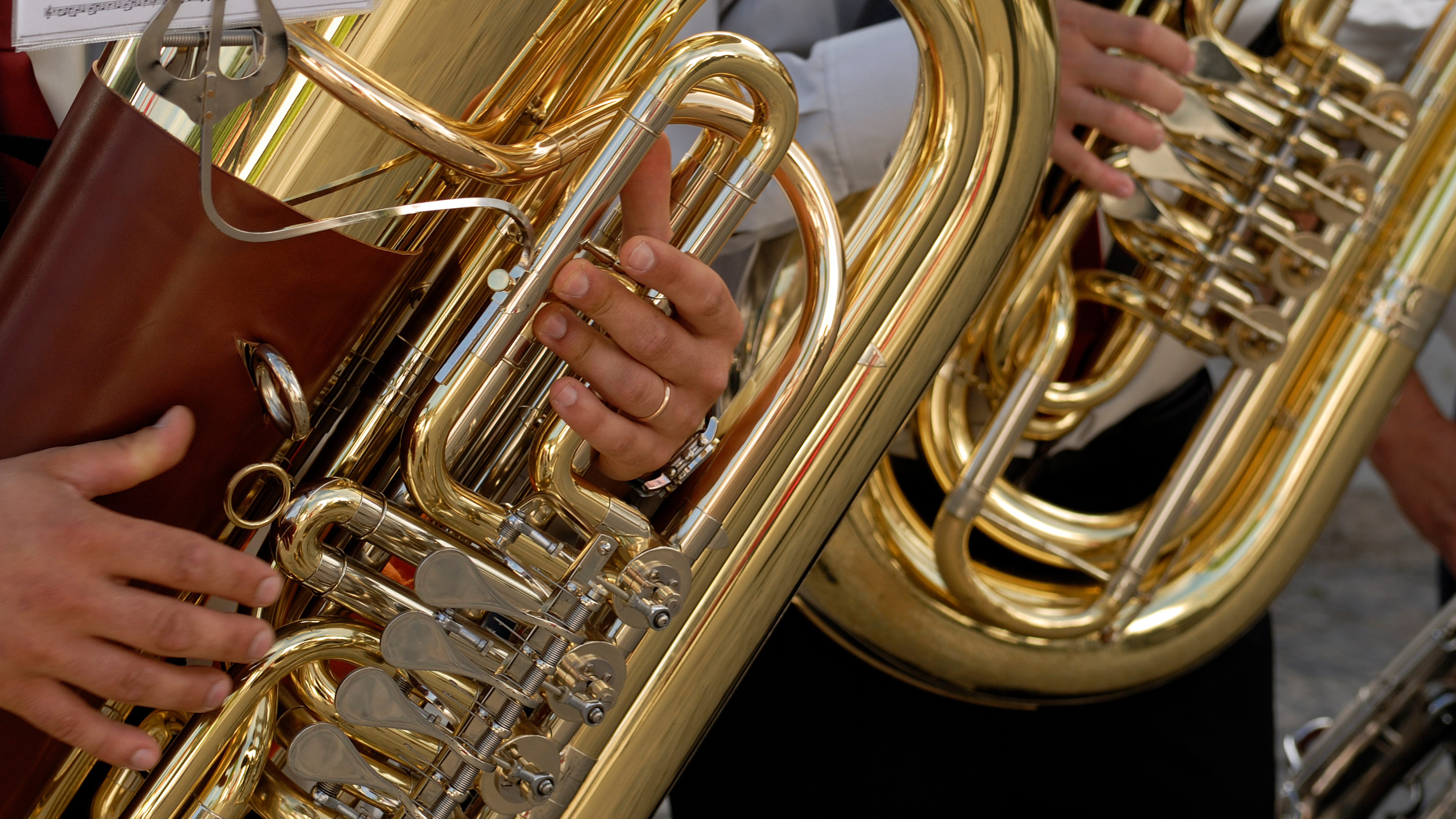 Close-up of musicians playing large brass instruments, with hands on valves and polished gold tubas reflecting light during a live band performance.