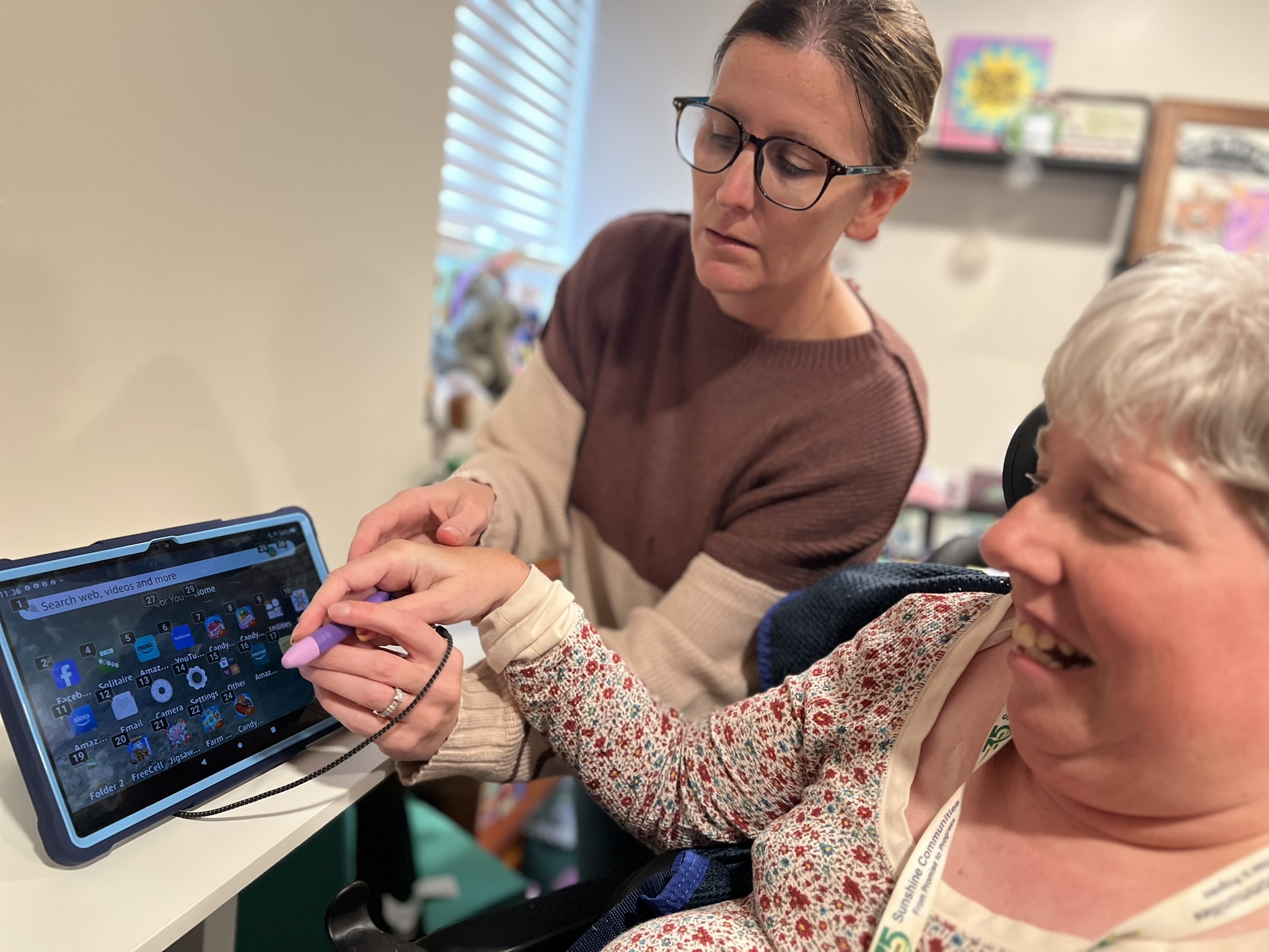 Beth uses a stylus to navigate a tablet with support from a Sunshine Communities staff member.