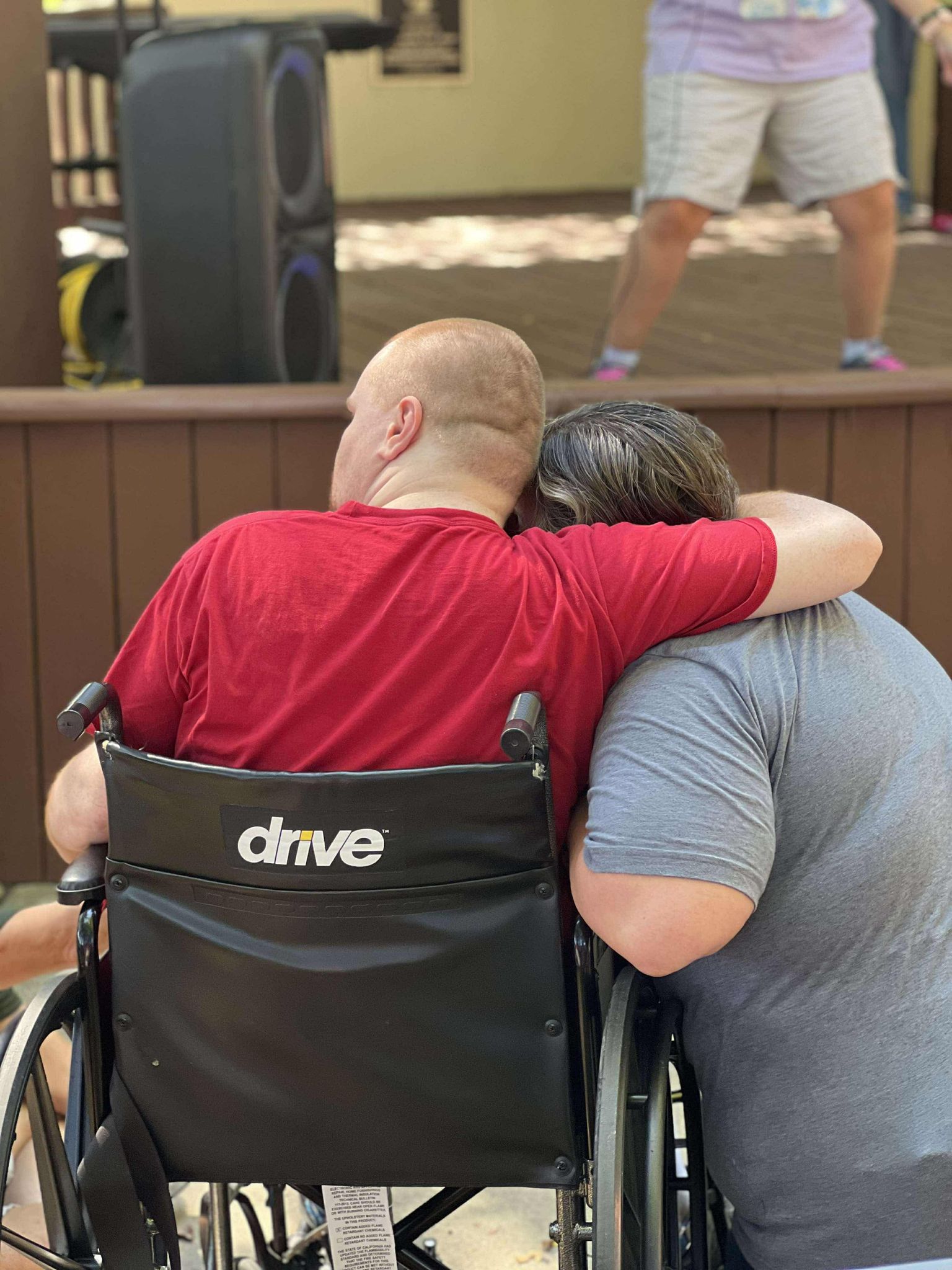 Blurred and partially obscured photo of a laptop keyboard and screen with text, layered over an image of a person in a wheelchair, creating a distorted, abstract effect.