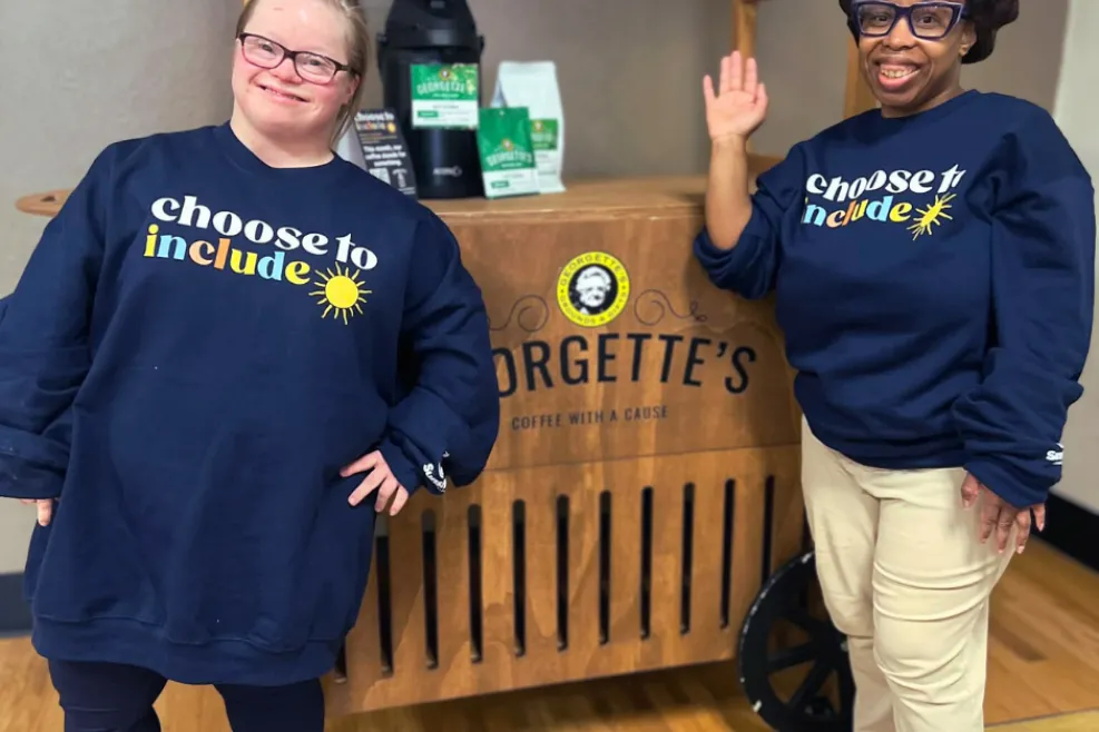 Two women smile in navy sweatshirts that read “Choose to Include.”
