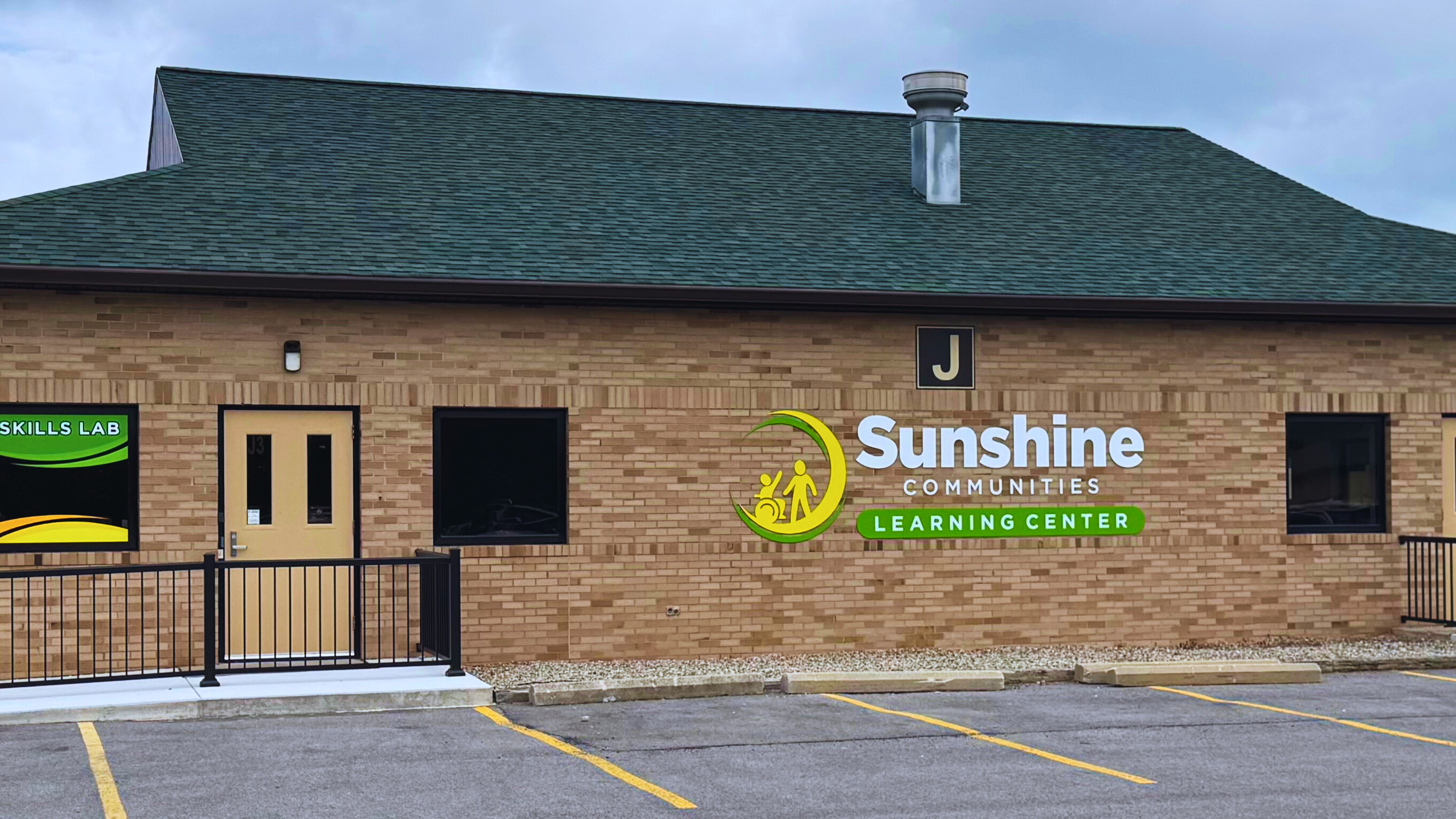 Exterior view of Sunshine Communities Learning Center building, featuring accessible entrance, designated parking, and bold signage with the organization's logo.