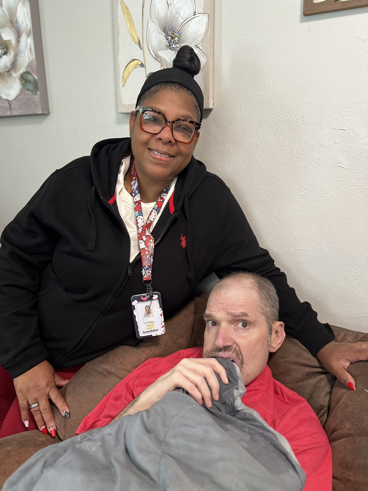 An individual sits comfortably in his recliner with a familiar Direct Support Professional beside him.
