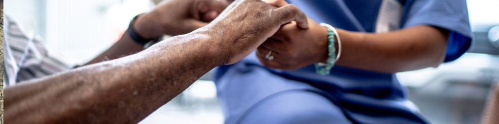 Alt Text: "Close-up of a caregiver in blue scrubs gently holding the hands of an elderly individual, symbolizing compassion, care, and support in a healthcare setting."