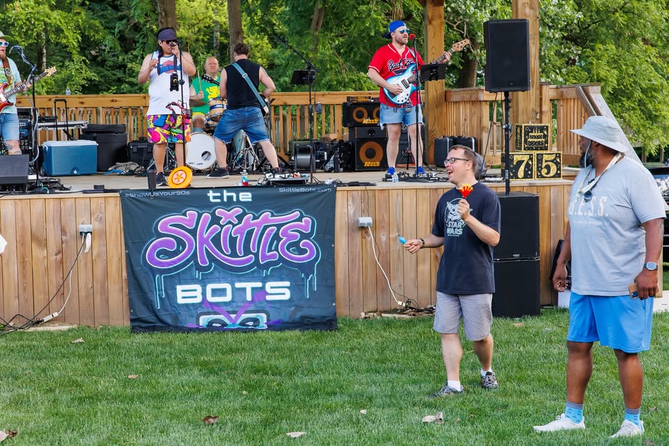 The Skittle Bots perform live during the Sounds of Sunshine Concert Series at Sunshine Communities as attendees enjoy music and activities in front of the outdoor stage.
