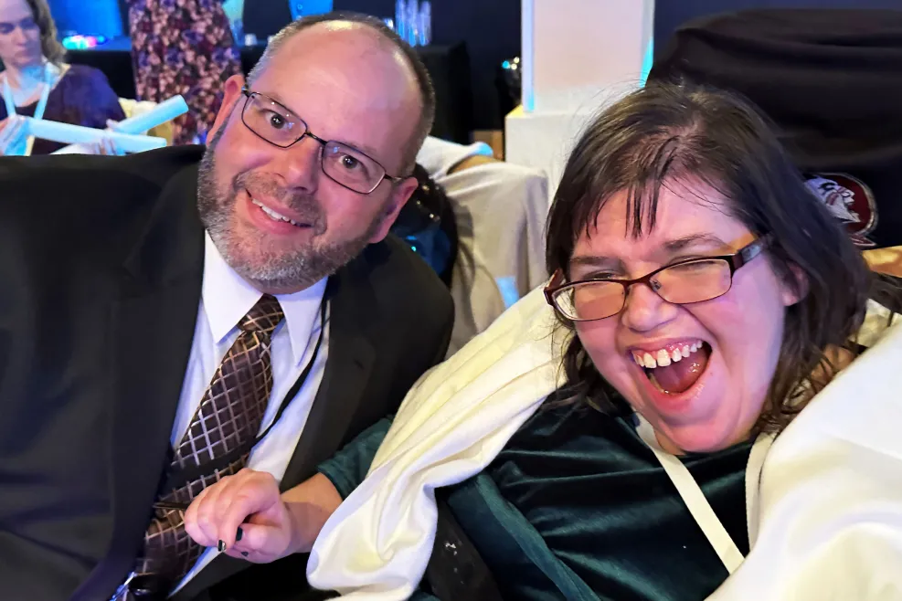 Smiling man and woman seated in a wheelchair, radiating happiness.