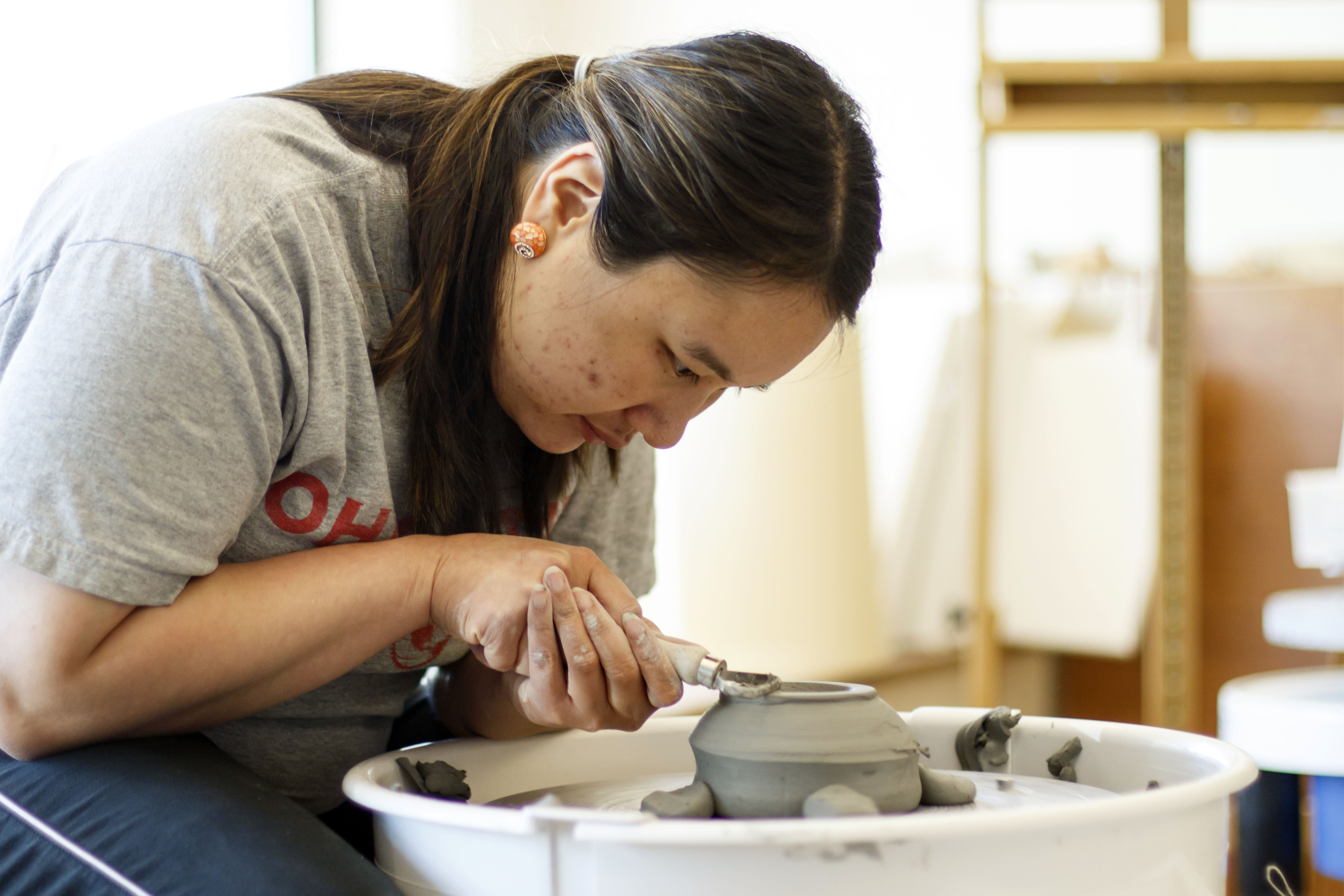 "An artist focusing intently while shaping a clay pot on a pottery wheel, working with great precision in an art studio.