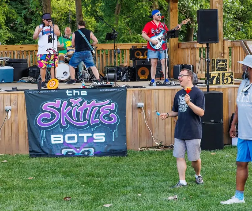 The Skittle Bots perform live during the Sounds of Sunshine Concert Series at Sunshine Communities as attendees enjoy music and activities in front of the outdoor stage.