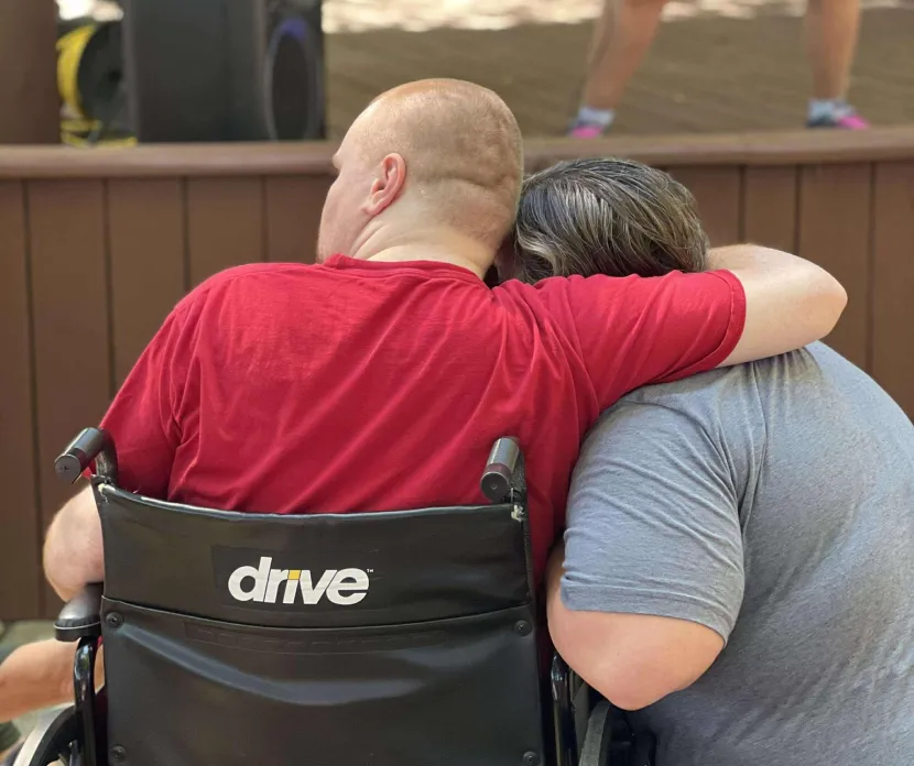 Blurred and partially obscured photo of a laptop keyboard and screen with text, layered over an image of a person in a wheelchair, creating a distorted, abstract effect.