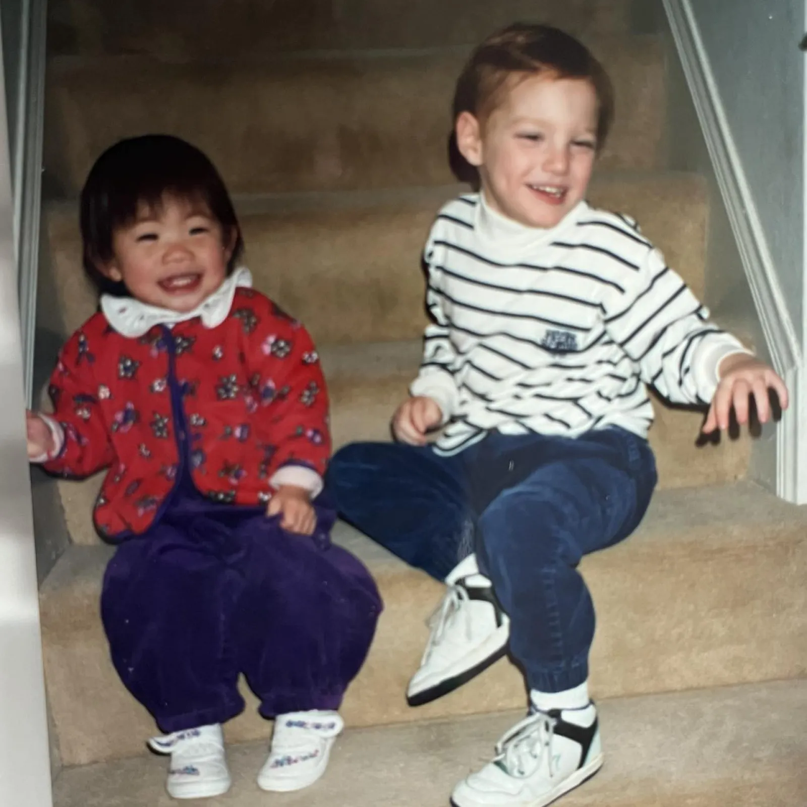 Two young children sit side by side on stairs.