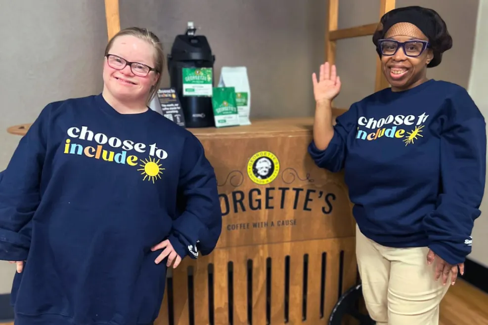 Two women smile in navy sweatshirts that read “Choose to Include.”