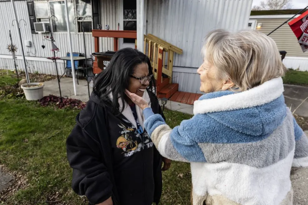 A Sunshine Communities volunteer gently greets an older woman outside her home in Toledo, Ohio, during a Mobile Meals delivery, sharing a warm and personal moment of connection.