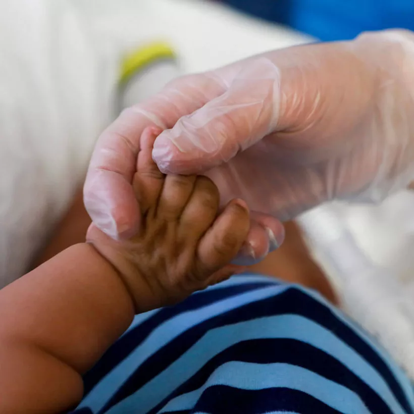 A Gloved Hand Holding a Baby's Hand