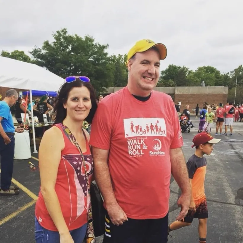 Two individuals in red shirts smiling for the camera after a race.