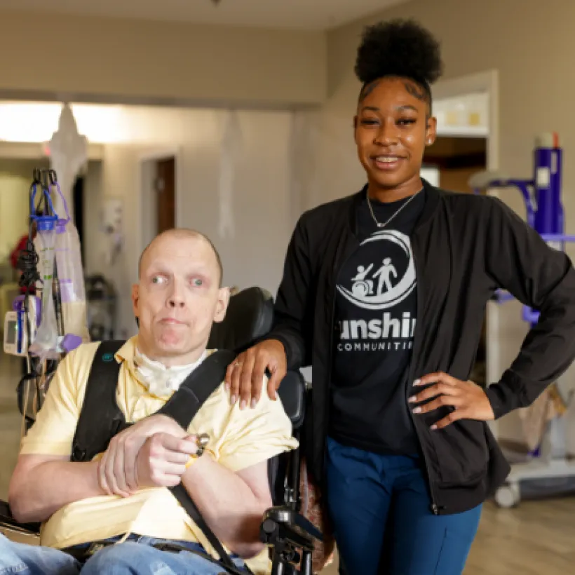 A woman in a Sunshine shirt beside a person she is assisting