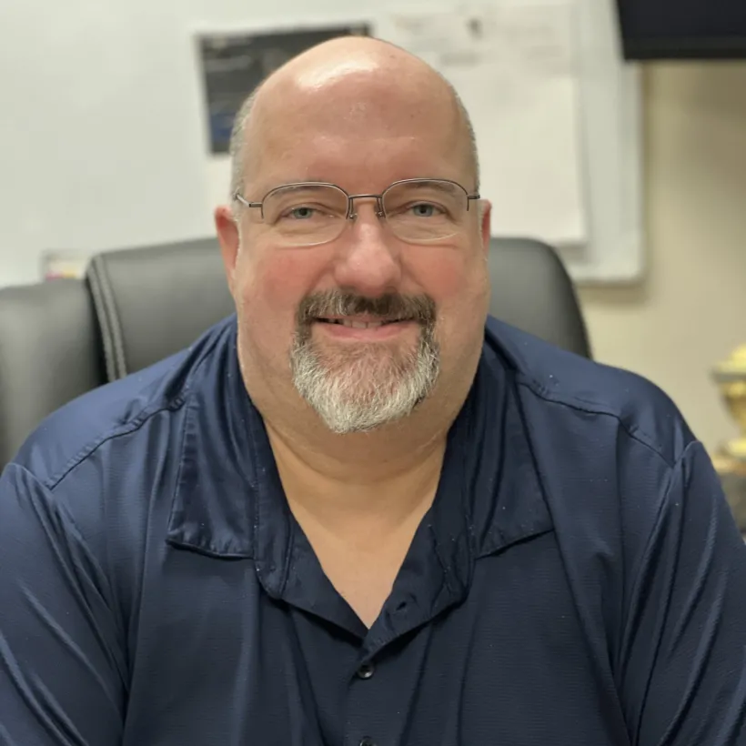 Rob Gasser smiling in an office setting wearing a navy shirt and glasses with Sunshine Communities badge visible