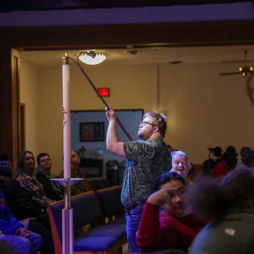A participant lights the Paschal candle during a Spiritual Life service at Sunshine Communities in Toledo, Ohio, as fellow attendees watch in a welcoming worship space.