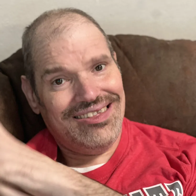 An individual supported by Sunshine Communities smiles while relaxing in his recliner at home.