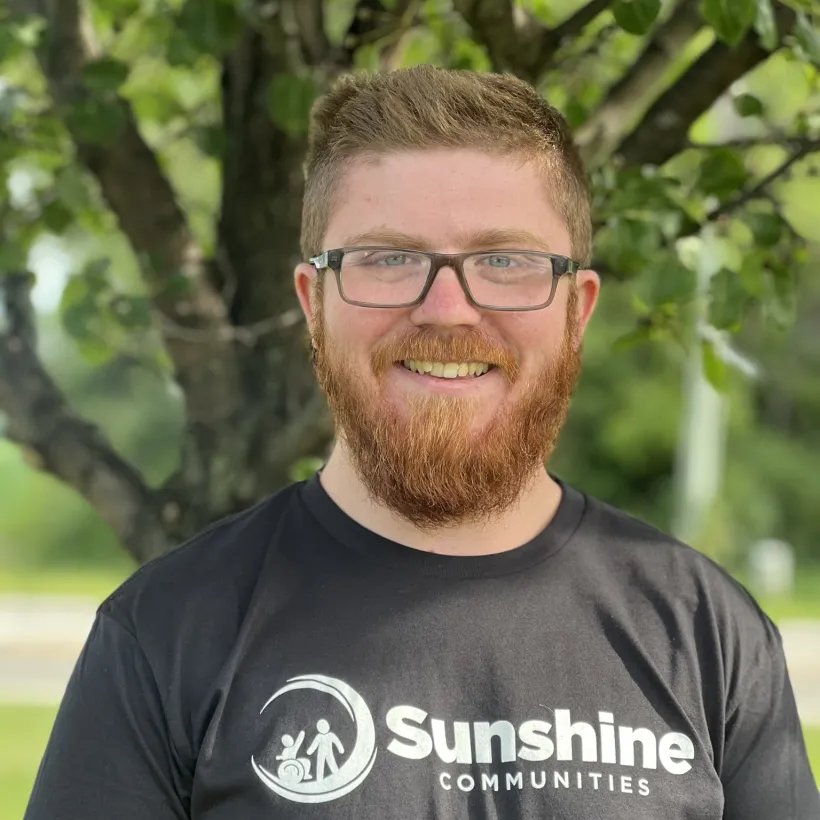 Sunshine Communities transportation driver outdoors wearing a Sunshine Communities shirt.